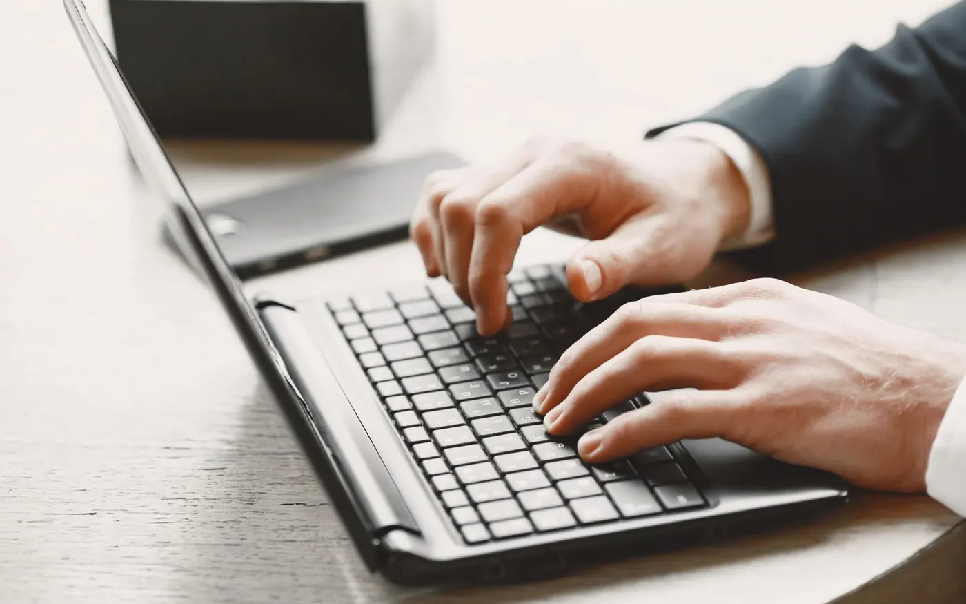 Manos de un asesor trajeado escribiendo en el teclado de un ordenador portátil